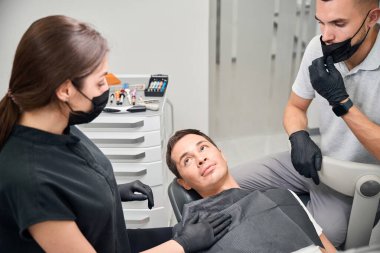 Diş tedavisinden ya da diş implantasyonundan, estetik dişçilikten önce gergin hisseden erkek hastayı sakinleştiren diş teknisyenlerinden oluşan bir ekip.