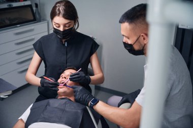 Ofislerinde çalışan iki deneyimli diş teknisyeni, erkek müşteriye diş tedavisi yapan profesyoneller, rutin diş sağlığı kontrolü.