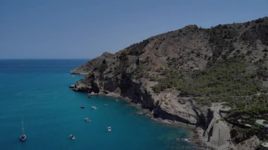 Hava görüntüsü kayalık kayalıkların yakınındaki demirde huzur içinde yüzen tekneleri yakalıyor. Bereketli bitki örtüsü ve sakin okyanus huzurlu bir yaz ortamı yaratır..
