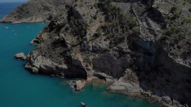 İspanya, Costa Blanca 'da sakin bir kıyı şeridini görüntüler. Birkaç küçük tekne, kayalık kayalıkların yakınındaki sakin suları doldurarak gün boyunca huzurlu bir atmosferi çağrıştırıyor..