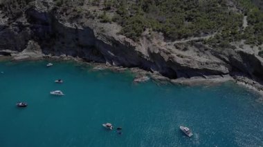 Akdeniz 'de kayalık bir kıyı şeridinin yanında yavaşça yüzen birden fazla teknenin olduğu sakin bir manzara. Sakin okyanus suları güneşli bir gündüz saatinin sakin havasını yansıtır..