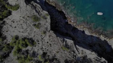 Huzurlu bir tekne Akdeniz 'in sakin sularında kayalık kıyılar ve yemyeşil bitki örtüsüyle çevrili bir şekilde süzülür. Gündüzün dinginliği, doğayla barışı çağrıştırıyor..