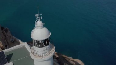 İki yetişkin, deniz fenerinin kıyısındaki bir uçurumun kenarında huzur içinde duruyor. Huzurlu okyanus manzarası ve güneş paneli İspanya 'nın Costa Blanca kentindeki sakin bir gündüz kuşağını yansıtıyor..