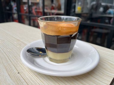 Güneşli bir sabahta karıştırılmaya ve tadını çıkarmaya hazır sütlü kahve. Acı kahve ve tatlandırılmış yoğunlaştırılmış süt. Bir dükkan ya da kafe içeceği menüsü. Bulanık arkaplan.