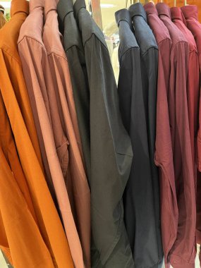 Askıya asılmış çeşitli gömlekler. Mağazada renkli yakalı gömlekler sergileniyor. Kumaşın dokusu pürüzsüz ve giyimi rahat. Tasarım için gömlek modeli. kumaş renk kombinasyonu.