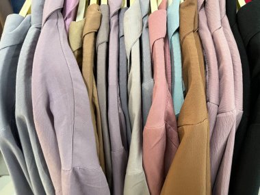 Askıya asılmış çeşitli gömlekler. Mağazada renkli yakalı gömlekler sergileniyor. Kumaşın dokusu pürüzsüz ve giyimi rahat. Tasarım için gömlek modeli. kumaş renk kombinasyonu.