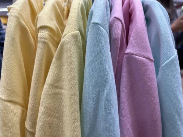 Neat rows of t-shirts with hangers. Colorful t-shirts are ready to be displayed to customers. A variety of soft and smooth cotton fabrics. Hangers for display. Bright colored fabric background concept