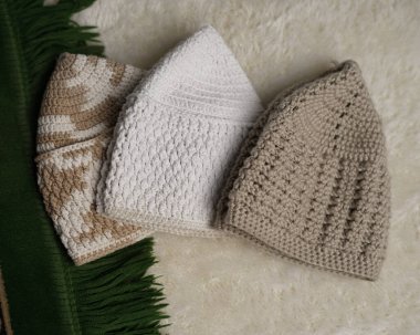 Songkok şapkaları koleksiyonu, Müslüman erkekler tarafından takılan dekoratif İslami başlıklar, farklı açılardan beyaz kürk halı arka planında izole edilmiş. Songkok elle bağlanmış Ramadhan Ramazan Bayramı 'ndan yapılır.