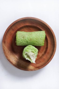 Ahşap bir tabakta 'Dadar Gulung' adı verilen geleneksel Endonezya yemekleri, rendelenmiş hindistan cevizi ve sıvı palmiye şekeriyle dolu eliptik bir pasta, beyaz bir zemin üzerinde izole edilmiş Dadar yuttu üst görünümü.