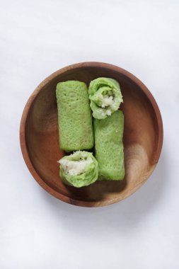 Ahşap bir tabakta 'Dadar Gulung' adı verilen geleneksel Endonezya yemekleri, rendelenmiş hindistan cevizi ve sıvı palmiye şekeriyle dolu eliptik bir pasta, beyaz bir zemin üzerinde izole edilmiş Dadar yuttu üst görünümü.