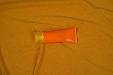 Turuncu kumaş arka planda izole edilmiş güneş kremi tüpü. Vücut bakımı güzellik tedavi konsepti