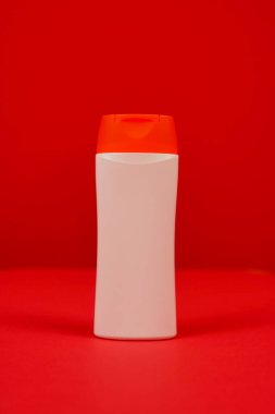 Kırmızı arka planda kapalı kapaklı plastik şampuan şişesi. Tasarımın için MockUp şablonu. Kozmetik ürünler için boş ve temiz ambalaj. Dosya kırpma yolu içeriyor.