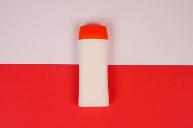 Kırmızı ve beyaz arka planda kapalı kapaklı plastik şampuan şişesi. Tasarımın için MockUp şablonu. Kozmetik ürünler için boş ve temiz ambalaj. Dosya kırpma yolu içeriyor.