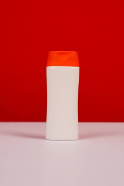 Kırmızı ve beyaz arka planda kapalı kapaklı plastik şampuan şişesi. Tasarımın için MockUp şablonu. Kozmetik ürünler için boş ve temiz ambalaj. Dosya kırpma yolu içeriyor.