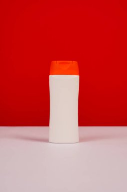 Kırmızı ve beyaz arka planda kapalı kapaklı plastik şampuan şişesi. Tasarımın için MockUp şablonu. Kozmetik ürünler için boş ve temiz ambalaj. Dosya kırpma yolu içeriyor.