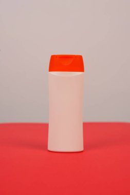 Kırmızı ve beyaz arka planda kapalı kapaklı plastik şampuan şişesi. Tasarımın için MockUp şablonu. Kozmetik ürünler için boş ve temiz ambalaj. Dosya kırpma yolu içeriyor.