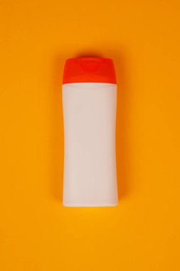 Turuncu arka planda kapalı kapaklı plastik şampuan şişesi. Tasarımın için MockUp şablonu. Kozmetik ürünler için boş ve temiz ambalaj. Dosya kırpma yolu içeriyor.