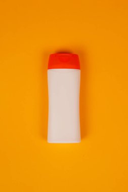 Turuncu arka planda kapalı kapaklı plastik şampuan şişesi. Tasarımın için MockUp şablonu. Kozmetik ürünler için boş ve temiz ambalaj. Dosya kırpma yolu içeriyor.