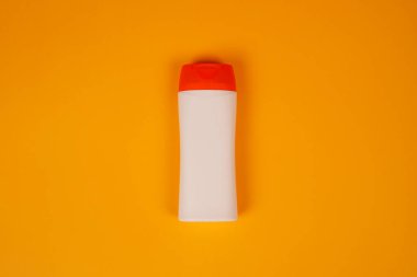 Turuncu arka planda kapalı kapaklı plastik şampuan şişesi. Tasarımın için MockUp şablonu. Kozmetik ürünler için boş ve temiz ambalaj. Dosya kırpma yolu içeriyor.