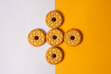 Beyaz ve turuncu arka planda çilekli bisküviler, yüzeylerinde dairesel kalp motifi ile süslenmiş. Yüksek çözünürlüklü fotoğraf.