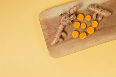 Taze zerdeçal kökü ve sarı arka planda izole edilmiş ahşap tabakta dilimler. Yüksek çözünürlüklü fotoğraf.