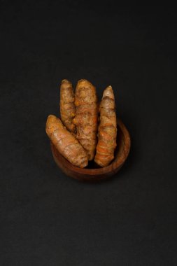 Siyah arka planda izole edilmiş ahşap tabakta taze zerdeçal kökleri. Yüksek çözünürlüklü fotoğraf.