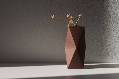 Çiçekler mukavva bir vazoda beyaz bir zemin üzerinde samandan yapılmıştır.