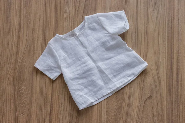 Children\'s linen clothes. White linen shirt on a wooden background. Top view