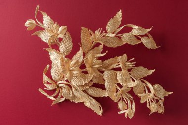 Yapraklı ve çiçekli dal samandan yapılmıştır. Kırmızı arka planda saman süslemesi. Dekorasyon. Parça yakın plan