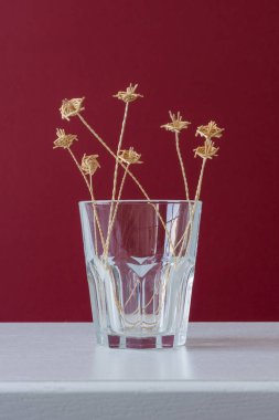 Kırmızı arka planda samandan yapılmış bir buket çiçekli cam bir vazo.