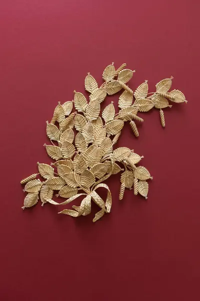 The branch with leaves is made of straw. Straw wall decoration. The products are made of straw. Decoration of straw on a red background