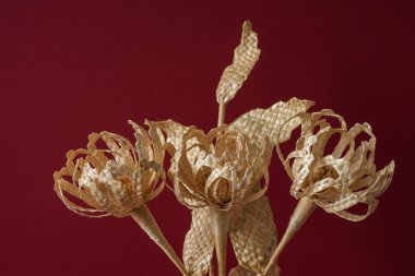 Kırmızı arka planda samandan yapılmış bir buket çiçekli cam bir vazo..