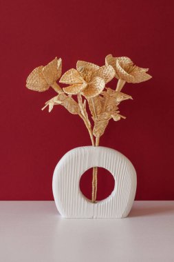 Kırmızı arka planda samandan yapılmış bir buket çiçekli ahşap bir vazo. Samandan örgü