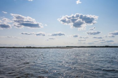 Güneşli bir günde gölün yüzeyinde dalgalar, mavi gökyüzü ve beyaz bulutlar..