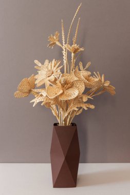 Çiçekler gri bir arkaplanda samandan yapılmıştır. Çiçekler karton bir vazoda samandan yapılmıştır. Samandan örgü
