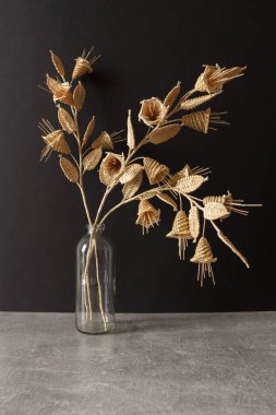 Siyah arka planda samandan yapılmış bir buket çiçekli cam bir vazo. Samandan örgü