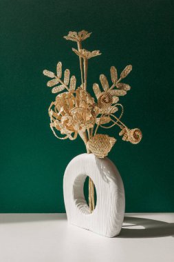 Yeşil arka planda samandan yapılmış bir buket çiçekli ahşap bir vazo. Samandan örgü