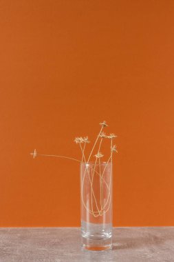 Turuncu arka planda samandan yapılmış bir buket çiçekli cam bir vazo.