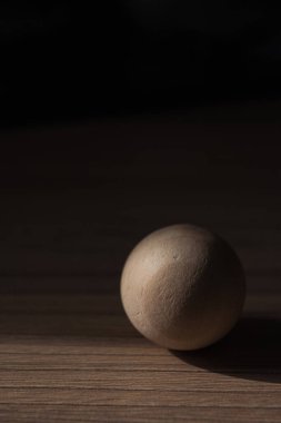 Ahşap bir arka planda güneş ışığıyla aydınlatılmış ahşap küre. Işık ve gölge oyunu. Geometrik formlu soyut minimal sahne. 