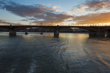 Gün batımının arkaplanına karşı nehrin üzerindeki köprü. Akşam gökyüzünde bulutlar.