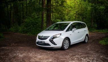 Yeşil yapraklı bir ormana park edilmiş beyaz aile arabası..