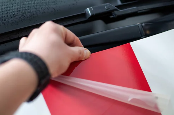 A man\'s hand gluing self-adhesive stripes on a car from red foil. Fast stripe decals on car.