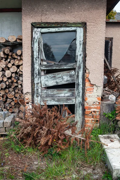 Old ruined wooden door with broken window and fallen plaster on garden house.