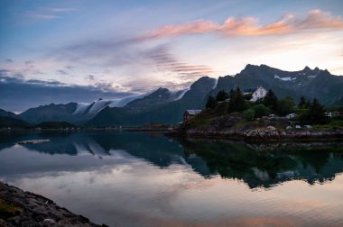 Norveç 'teki kutup gecesinde akşam üstü gün batımı. Deniz ve bulutlu yüksek kayalık dağlar.