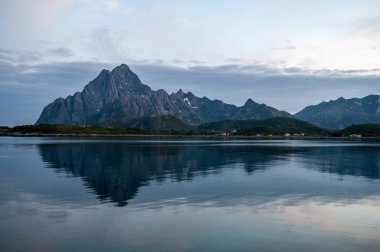 Norveç 'teki kutup gecesinde akşam üstü gün batımı. Deniz ve bulutlu yüksek kayalık dağlar.