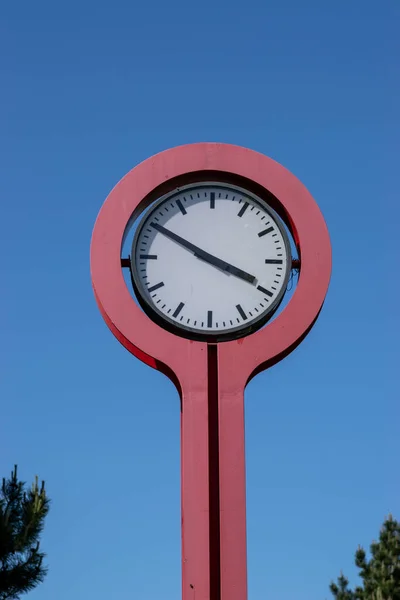 stock image An old red metal hand clock with a white dial placed outside on the street.