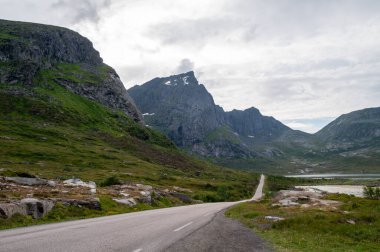 Fiyort körfezindeki yüksek dağların kıyısındaki yol. Lofoten, Norveç.