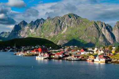 Norveç 'te Lofoten Adaları' nda bir fiyordun kıyısındaki Reine kasabası. Kuzey Avrupa 'da güneşli kayalık dağlar.