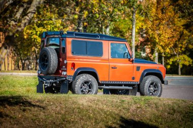 Brno, Çek Cumhuriyeti - 15 Ekim 2023: Orange Land Rover Defender 90 SUV Sonbahar ağaçlarının altına park edildi.