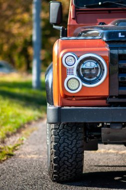Brno, Çek Cumhuriyeti - 15 Ekim 2023: Orange Land Rover Defender 90 SUV Sonbahar ağaçlarının olduğu yola park etti. Ön ışık detayı.